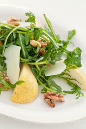 Auf dem Bild ist ein Salat mit Rucola, Birnenscheiben, Walnüssen und Käsestücken zu sehen.