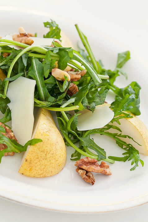 Auf dem Bild ist ein Salat mit Rucola, Birnenscheiben, Walnüssen und Käsestücken zu sehen.