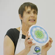 Auf dem Bild ist eine Frau zu sehen, die einen Käse hält und begeistert darüber spricht.