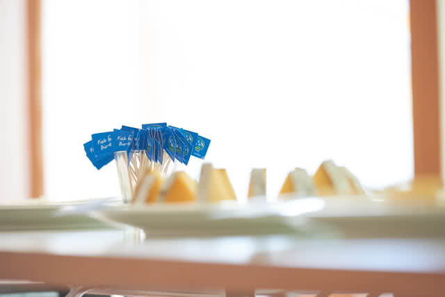 The image displays several small blue flags set into portions of our artisanal Allgäu cheese, highlighting the region’s time-honored dairy craftsmanship and the natural care that goes into every wheel.