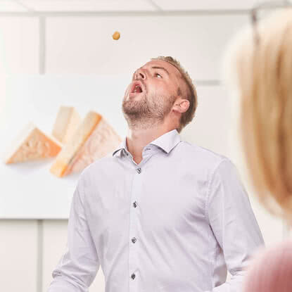 Auf dem Bild ist ein Mann zu sehen, der nach einem kleinen Snack greift, während sich eine andere Person im Hintergrund befindet.