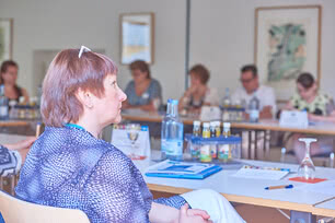Auf dem Bild ist eine Gruppe von Personen während eines Meetings oder einer Besprechung in einem Konferenzraum zu sehen.