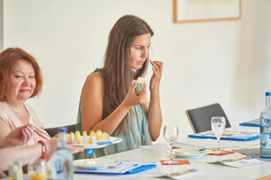 Auf dem Bild sind mehrere Personen zu sehen, die an einem Tisch sitzen und anscheinend an einer Verkostung oder einem gemeinsamen Essen teilnehmen.