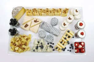 Auf dem Bild ist eine vielfältige Auswahl von Käse, Oliven, Früchten und Desserts auf einem Tisch präsentiert.