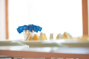 Auf dem Bild sind bunte Fähnchen zu sehen, die auf Käse oder ähnlichen Snacks stecken.