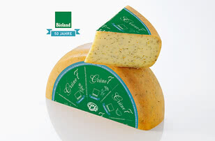 Auf dem Bild ist ein Stück Käse mit einer grünen Verpackung zu sehen, das mit dem Bioland-Logo und dem Jubiläumslabel