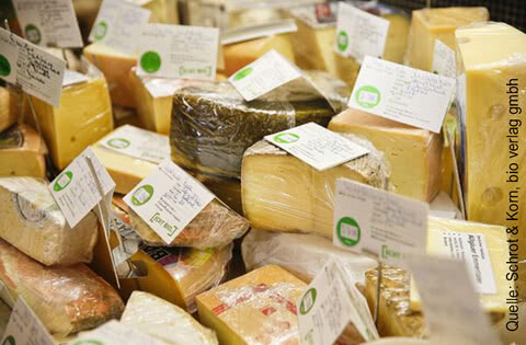 Auf dem Bild sind viele verschiedene Käsesorten zu sehen, die in Verpackungen mit Etiketten angeordnet sind.