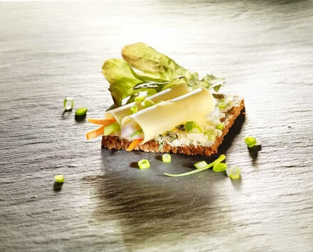 Auf dem Bild ist ein belegtes Brot mit Käse, frischem Gemüse und Kräutern zu sehen.