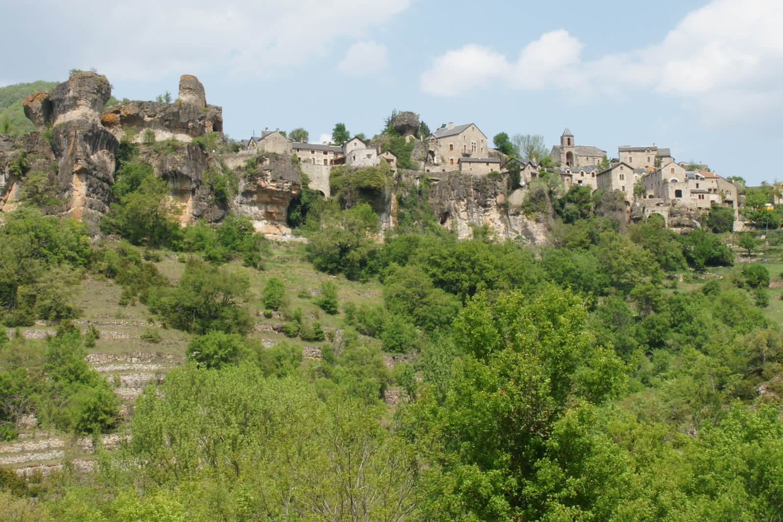 Auf dem Bild ist ein historisches Dorf zu sehen, das auf einem bewaldeten Hügel liegt.
