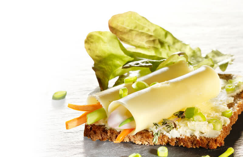 Das Bild zeigt ein belegtes Brot mit Käse, Gemüse und frischen Kräutern.