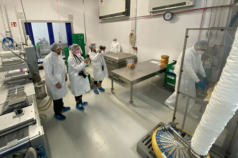 Auf dem Bild sind mehrere Personen in Schutzkleidung zu sehen, die einen Lebensmittelverarbeitungsbereich betreten und Fotografien machen.