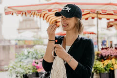 Auf dem Bild ist eine fröhliche Frau zu sehen, die in einem Blumenmarkt steht und gerade etwas isst.