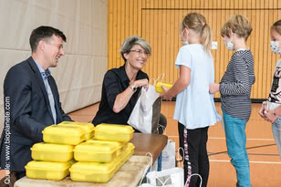Auf dem Bild sind Erwachsene und Kinder zu sehen, die in einer Sporthalle zusammenkommen, um Lebensmittel oder Geschenke auszuhändigen.
