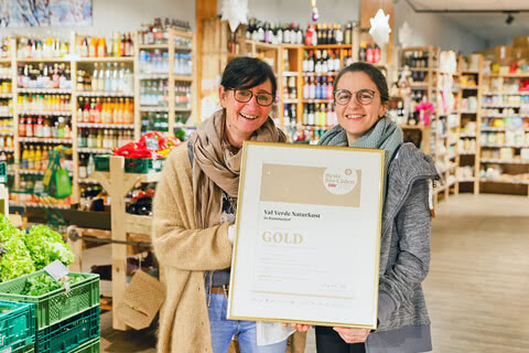 Auf dem Bild sind zwei Frauen zu sehen, die stolz eine Auszeichnung für den besten Bio-Laden 2022,