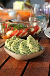 Auf dem Bild ist eine Schale mit Kräuterbutter zu sehen, umgeben von verschiedenen Salatzutaten.