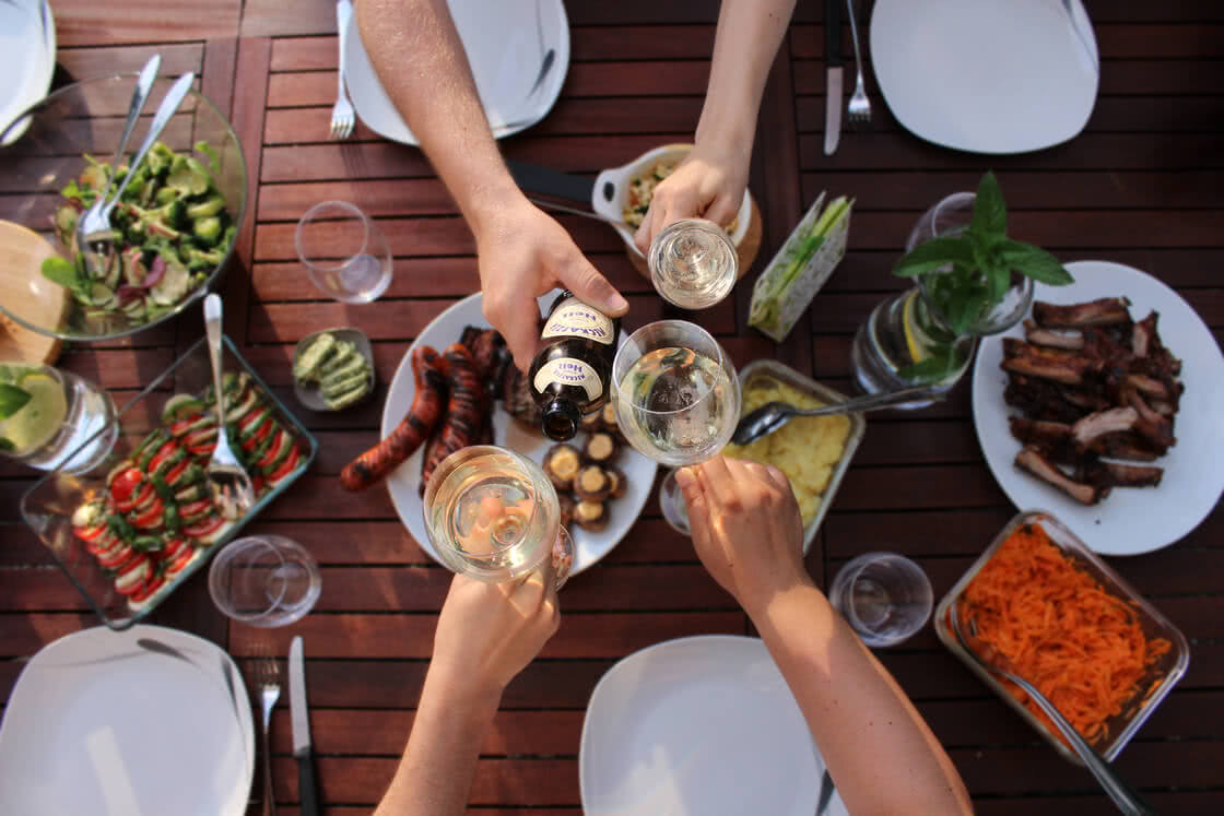 Auf dem Bild ist eine fröhliche Zusammenkunft zu sehen, bei der mehrere Personen Essen und Getränke teilen und anstoßen.