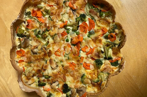 Auf dem Bild ist eine herzhafte Gemüsequiche mit Brokkoli, Karotten und Mandelscheiben zu sehen.