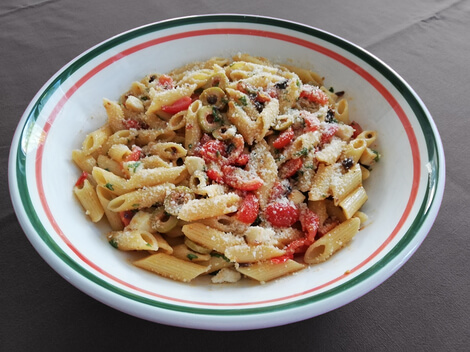 Auf dem Bild ist eine Schüssel mit Penne-Pasta, Tomaten, Oliven und Käse zu sehen.