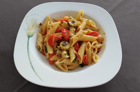 Auf dem Bild ist ein Teller mit Penne-Nudeln, Tomaten und eventuell weiteren Zutaten zu sehen.