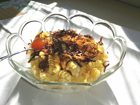 Auf dem Bild ist eine Schüssel mit Nudeln zu sehen, die mit frittierten Zwiebeln und einem rohen Eigelb garniert sind.