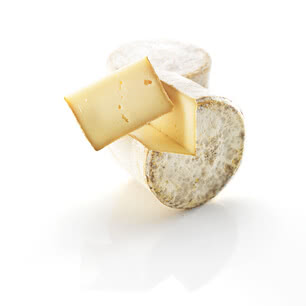 Das Bild zeigt ein Stück Käse, das teilweise aus einer runden Käseform herausgeschnitten ist.