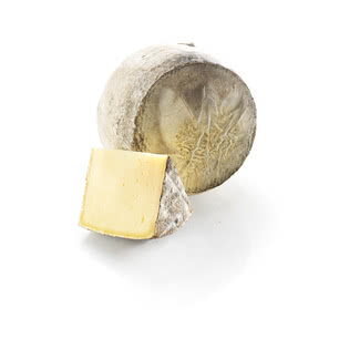 Auf dem Bild ist ein Stück Käse zusammen mit einem ungeschnittenen Käselaib zu sehen.