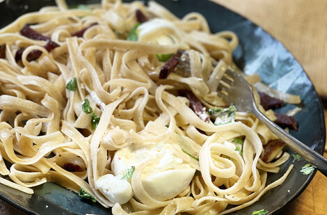 Auf dem Bild ist ein Teller mit Nudeln, Kräutern und kleinen Portionen von frischem Käse zu sehen.