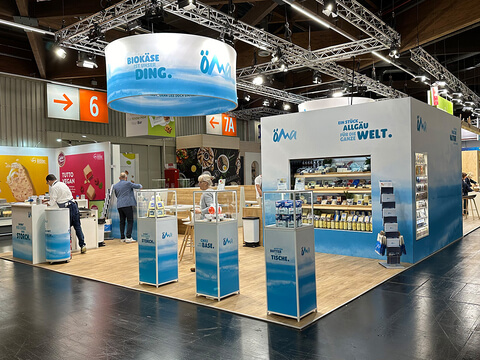 Auf dem Bild ist ein Stand auf einer Messe zu sehen, der regionale Biokäse-Produkte aus dem Allgäu präsentiert.