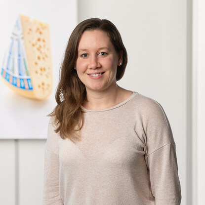 Auf dem Bild ist eine lächelnde Frau vor einem Hintergrund mit einem Käsemotiv zu sehen.