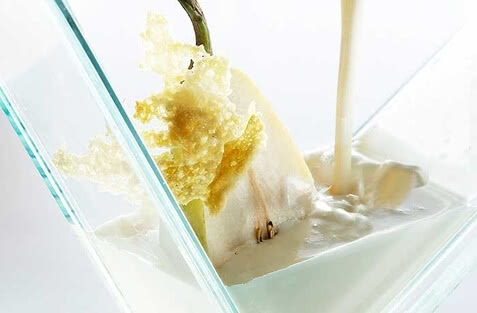 Auf dem Bild ist eine Kombination aus einer geschnittenen Frucht, möglicherweise Birne, die in einer cremigen Flüssigkeit liegt, während eine weitere Flüssigkeit darüber gegossen wird.