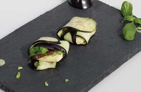 Auf dem Bild sind mit Auberginen und anderen Zutaten gefüllte Röllchen auf einem schwarzen Teller zu sehen.