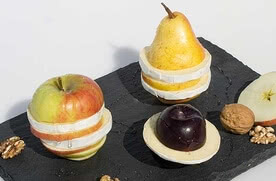 Auf dem Bild sind eine Apfel- und eine Birnenkomposition zu sehen, die aus verschiedenen Obststücken und Käse bestehen.