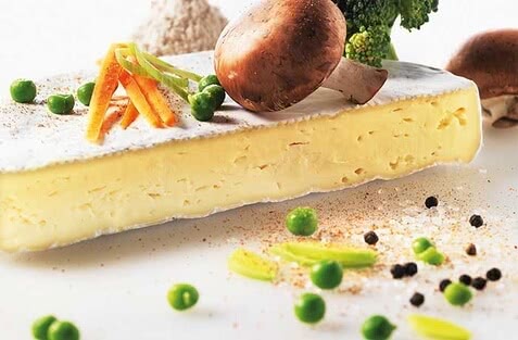 Auf dem Bild ist ein Stück Käse mit verschiedenen Gemüsebeilagen, darunter Erbsen, Karotten, Pilze und Brokkoli, zu sehen.