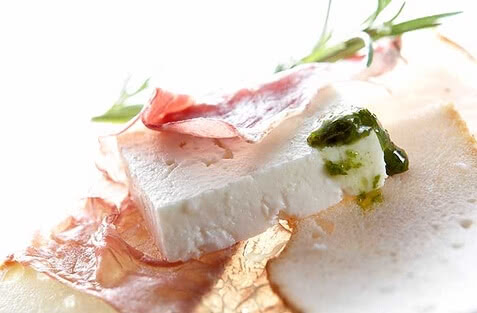 Auf dem Bild sind Käse und Schinken, zusammen mit einer Kräutersoße und etwas Brot, ansprechend angerichtet zu sehen.