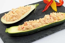 Auf dem Bild sind halbierte Zucchini zu sehen, die mit einer cremigen Füllung aus Fisch und Gemüse gefüllt sind.