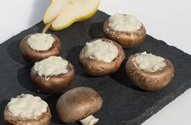 Auf dem Bild sind gefüllte Champignons mit einer cremigen Füllung zu sehen, neben einer halbierten Birne.