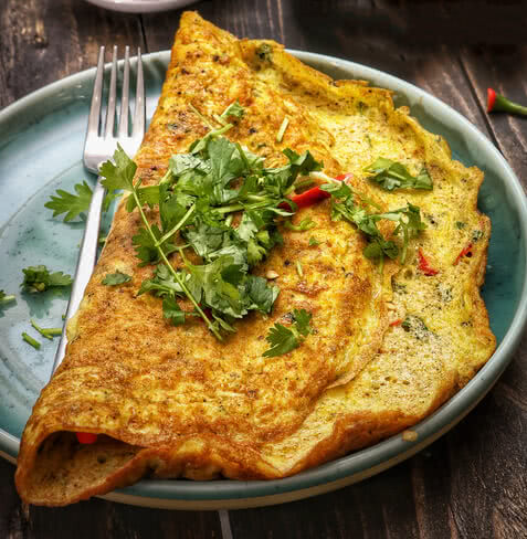 Auf dem Bild ist eine Omelette zu sehen, die mit frischen Kräutern und roten Paprikastücken garniert ist.